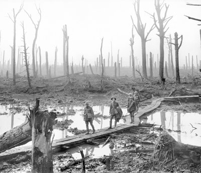 Vijf Australiërs, leden van een veldartilleriebrigade, die over een eendenbordpad over modder en water lopen tussen kale boomstammen in het verwoeste Chateau Wood, een deel van een van de slagvelden door Australian Photographer