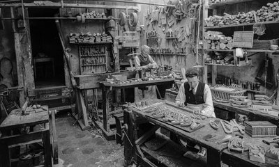 Ambachtslieden aan een werkbank in een werkplaats die kleine houten voorwerpen maken door Bernard F. Rogers