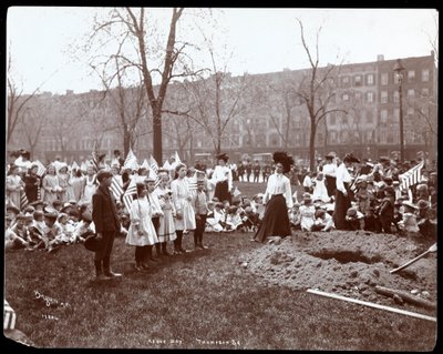 Volwassenen en kinderen met vlaggen staan rond een nieuw gegraven gat voor een boomplanting op Arbor Day in Tompkins Square Park, New York door Byron Company