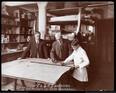 Portret van Henry en S.G. Lindeman met hun zoon of kleinzoon staande over winkeltekeningen voor een piano, 1910 door Byron Company