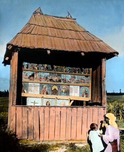 Roemenië, Bukovina, moeder met kind voor een kleine kapel met afbeeldingen van de Heiligen, circa 1920 door Carl Simon