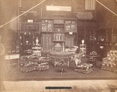 Tentoonstelling van S. Howard & Sons -- Hoofdgebouw, Collectie meubels, waaronder gestoffeerde stoelen, tafels, een open haard, kasten en schappen. Aan de muren hangen tapijten, en op tafels en planken staan vazen door Centennial Photographic Co.