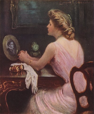 Vrouw zittend aan haar kaptafel kijkend naar een foto van een man, mogelijk haar echtgenoot of minnaar door Clarence F. Underwood