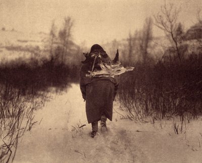 Op weg naar het kamp. Een apsaroke Indiaan die hout draagt in de sneeuw, in een klein winterkamp nabij een beek in de Pryor Mountains, Montana. Foto uit volume 4 van de encyclopedie gepubliceerd door Edward S. Curtis over de Indianen van Noord-Amerika. door Edward Sheriff Curtis