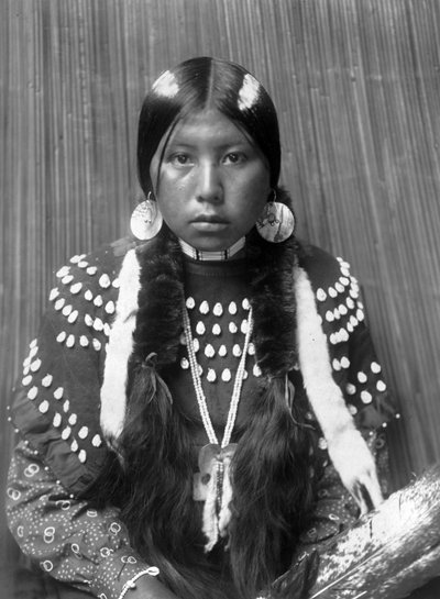 Kalispel Indiaanse vrouw, witte strepen geschilderd op haar, schelfschijf oorbellen, gekleed in dekenjurk versierd met elandstanden, c. 1910, foto Edward S. Curtis door Edward Sheriff Curtis