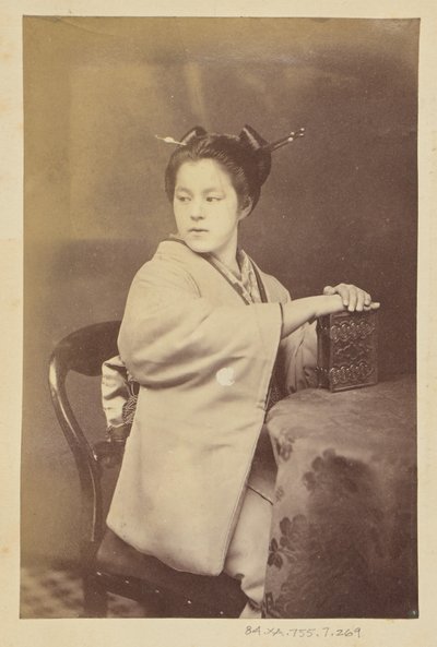 [Zittende Japanse vrouw die een cartes-de-visite album vasthoudt aan een tafel]. door Felice Beato
