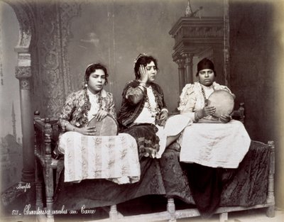 Portret van drie jonge Arabische zangers in etnische kleding met lange kettingen. Ze poseren in de studio, zittend. Twee van hen houden een tamboerijn vast door Félix Bonfils