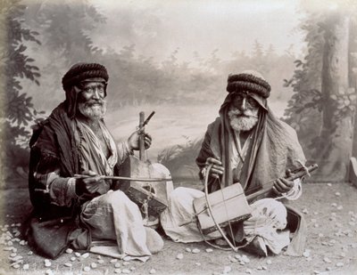Portret van twee Arabische muzikanten in eenvoudige etnische kleding. De oudere mannen poseren in de studio, zittend op de grond. Achter hen is een achtergrond van een boslandschap door Félix Bonfils