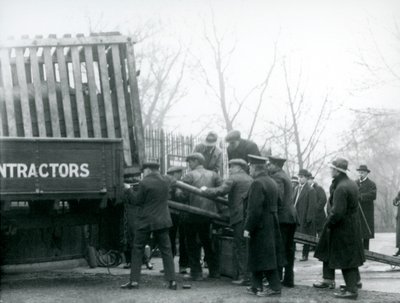 Een menigte toeschouwers staat erbij terwijl een neushoorn uit een vrachtwagen wordt gelost door verzorgers, London Zoo in 1924 door Frederick William Bond
