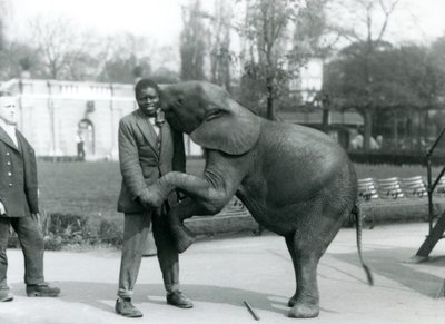Een jonge Afrikaanse Pygmee-olifant omhelst haar Afrikaanse trainer, terwijl de verzorger toekijkt, London Zoo, juli 1925 door Frederick William Bond