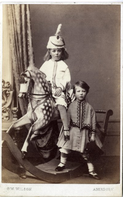 Jong meisje met hoed op schommelpaard met ander meisje erbij door George Washington Wilson