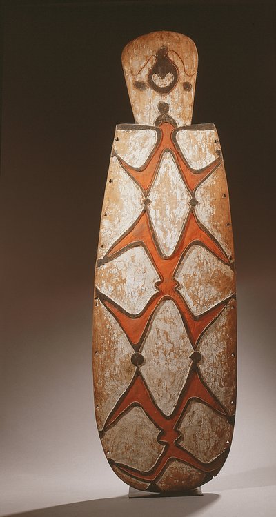 Ovale Asmat schild, gesneden in reliëf met gestileerde figuren, een masker bovenaan door Guinean New