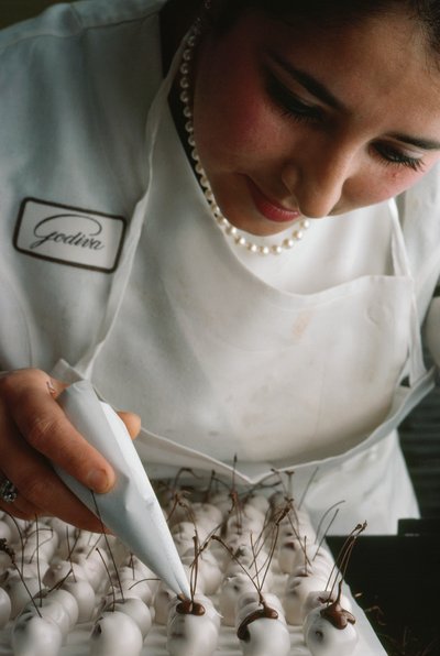 Een Godiva-chef bevestigt chocoladestelen aan met fondant bedekte kersen. Brussel, België. door James L Stanfield