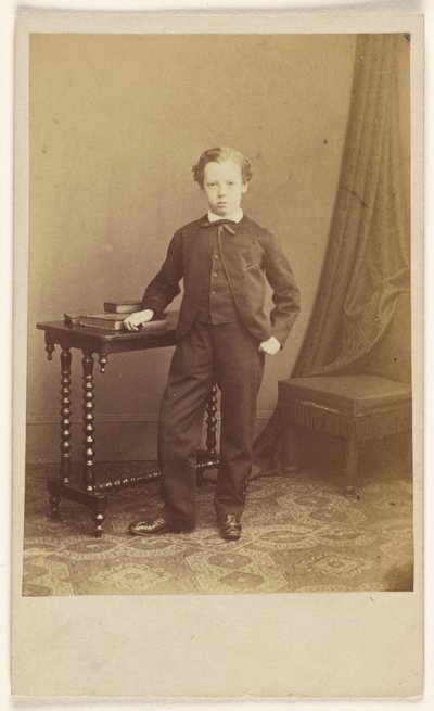 [Ongeïdentificeerd jongetje in pak staat bij een tafel met boeken erop]. door Joseph Brown