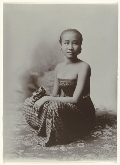 Studioportret van een zittende jonge Javaanse vrouw in een sarong met batik motief door Kassian Cephas