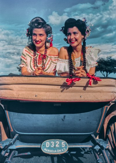 Jonge Nicaraguaanse vrouwen poseren in feestelijke kostuums en hoofdtooien achter in een koets door Luis Marden