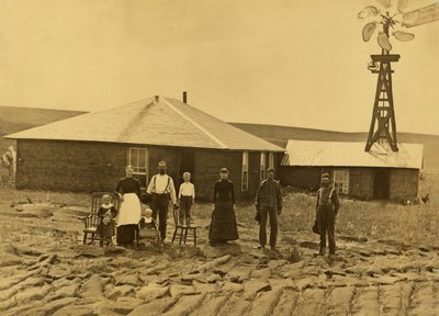 Familie van kolonisten, buiten hun zodenhuis met een windmolen op het dak van het aangrenzende gebouw in Custer County, Nebraska, ca. 1885 door Solomon D. Butcher