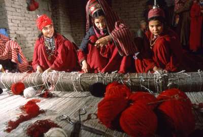 Turkoman stamvrouwen weven en trimmen knopen in de schering van een tapijt op een weefgetouw in een dorp door Thomas J. Abercrombie