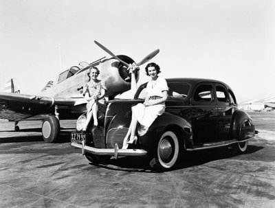 Californië: 1939 Twee Vrouwen Zitten op de Spatborden van een 1939 Lincoln Zephyr Sedan op een Vliegveld met een Eenmotorig Vliegtuig Geparkeerd Achter Hen (zw/w foto) door Unbekannt