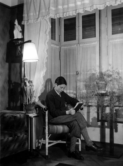 Een tiener zittend in een bourgeois interieur leest een boek, draagt korte broek en hoge sokken. 1915. Historische foto, vrouw lezend, ca. 1915 door Unbekannter Künstler