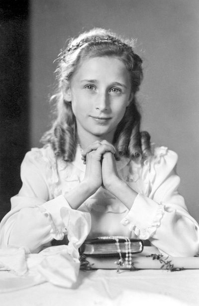 Christelijk meisje met gevouwen handen in gebedspositie met bijbel, rozenkrans en kaars (foto van communie). Fotografie rond 1932 door Unbekannt