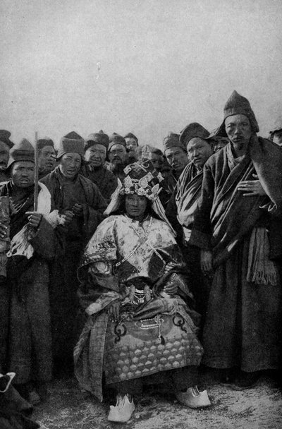 Tibet. Tovenaar in vol ornaat en een bewonderende groep monniken. 1920 door Unbekannt