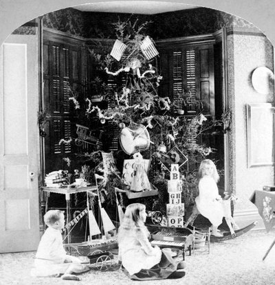 Kinderen verzameld aan de voet van de boom omringd door cadeaus op kerstochtend. door Unknown photographer