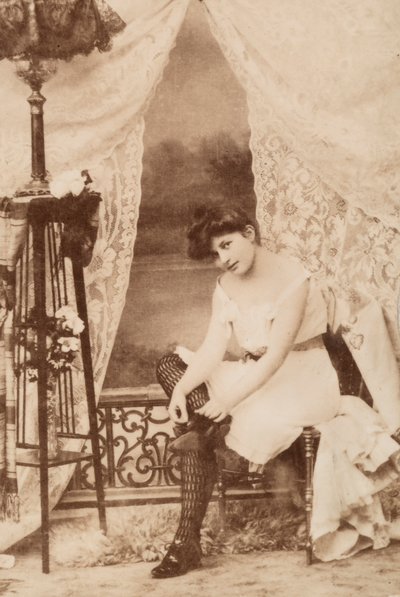 Portret van een jonge vrouw in intieme kleding, zittend terwijl ze haar schoen strikt door Unknown photographer