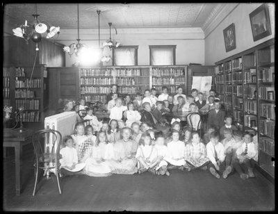 Groepsportret van kinderen in de leeszaal van een niet-geïdentificeerde vestiging van de Queens Borough Public Library, c.1910 door William Davis Hassler