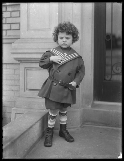 Kleine jongen in matrozenpak op de stoep van een appartementengebouw aan Vermilyea Avenue, ca. 1913 door William Davis Hassler