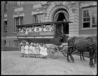 Kleine meisjes poseren in en voor een door paarden getrokken wagen, voor een onbekend gebouw, waarschijnlijk het Rooms-Katholieke Weeshuis, Kingsbridge, Bronx, ca. 1910 door William Davis Hassler