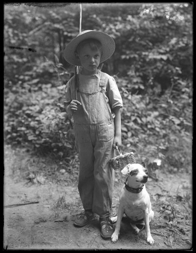 William Gray Hassler in strohoed en overall, met visstok en mand, geposeerd in het bos met een kleine hond (Bessie), 20 augustus 1911 door William Davis Hassler