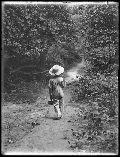 William Gray Hassler in strohoed en overall, met een hengel en mand, wandelend over een pad in het bos, 20 augustus 1911 door William Davis Hassler