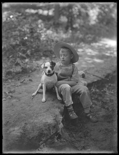 William Gray Hassler in strohoed en overall, zittend in het bos met een kleine hond (Bessie), 20 augustus 1911 door William Davis Hassler