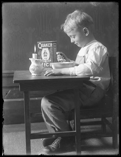 William Gray Hassler zittend aan een kleine tafel etend een kom Quaker gepofte rijst, ca.1912 door William Davis Hassler