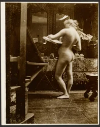 [vrouwelijk naaktmodel staand in studio met schetsboek].