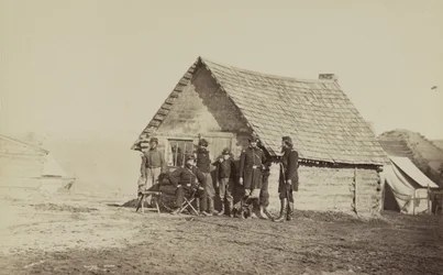 Een groep soldaten en twee jonge mannen, een Afro-Amerikaan, staan buiten blokhutkwartieren, 1861-65