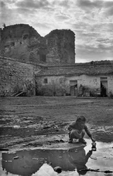 Jong meisje speelt met een papieren bootje in een plas omringd door modder, Venosa, Basilicata, Italië