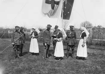 Een groep niet-geïdentificeerde officieren, verpleegsters en mannen van het 3e Australische Casualty Clearing Station verzameld onder een vlaggenmast met de Australische vlag (Australian Blue Ensign) en de Rode Kruis vlag
