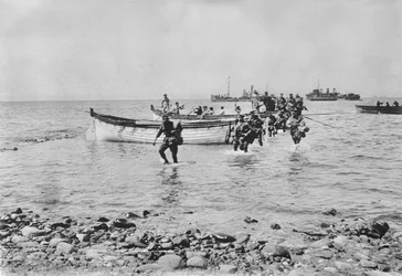 Australische soldaten die door het water waden terwijl ze aan land komen bij Anzac Cove, Gallipoli op 25 april 1915 na te zijn vervoerd in landingsboten vanaf grotere schepen op de achtergrond, 25 april 1915