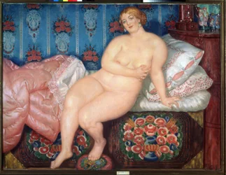 De schoonheid. Portret van een dikke blonde naakte vrouw, glimlachend, die een bescheiden gebaar maakt om haar borst te verbergen, half zittend op een onopgemaakt bed.