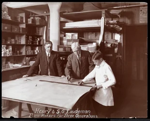 Portret van Henry en S.G. Lindeman met hun zoon of kleinzoon staande over winkeltekeningen voor een piano, 1910