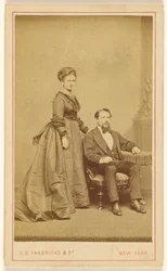 [Ongeïdentificeerd paar: vrouw staand, man met Vandyke baard zittend].