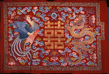 Een Chinese wandkleed van rode wol met een centraal karakter in goudkleurige draad geflankeerd door een feniks en een draak, 19e eeuw
