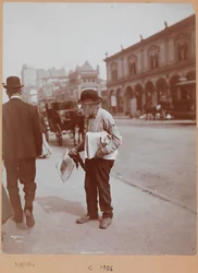 Een man die op de stoep van Broadway tussen 34th St. en 35th St. staat met de krant The Evening Telegram