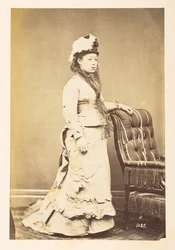 Japanse vrouw in Europese kleding, Volledig staand studiportret van een jonge Japanse vrouw in westerse kleding en hoed, Fotograaf: Onbekend Lucas Collectie: Fotografisch verslag van de wereldreis van Charles James en Morton P, Lucas