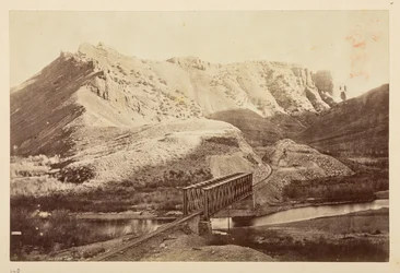Uitzichten op de Pacific Railway, van spoorlijn die een rivier oversteekt op een liggerbrug, met bergen daarachter