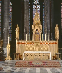 Hoogaltaar in neogotische stijl, omringd door 4 engelen die de instrumenten van de Passie van Christus dragen met een tabernakel bekroond door een rijkelijk versierde torenspits