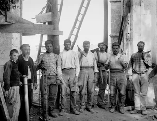 Het team van timmerlieden, werkend aan de restauratie van de Abdij van Septfontaines, Bourmont in Haute-Marne, poserend met hun gereedschap, bijl, zaag, loodlijn, regels en massa, rond 1890. Fotografie. Ducos Collectie