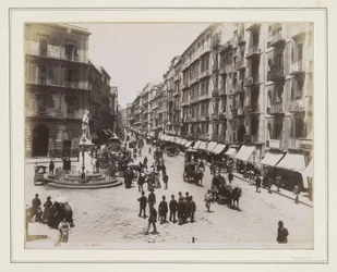 Gezicht op de Via Roma in Napels met een standbeeld, winkels, paardenkoetsen en voorbijgangers